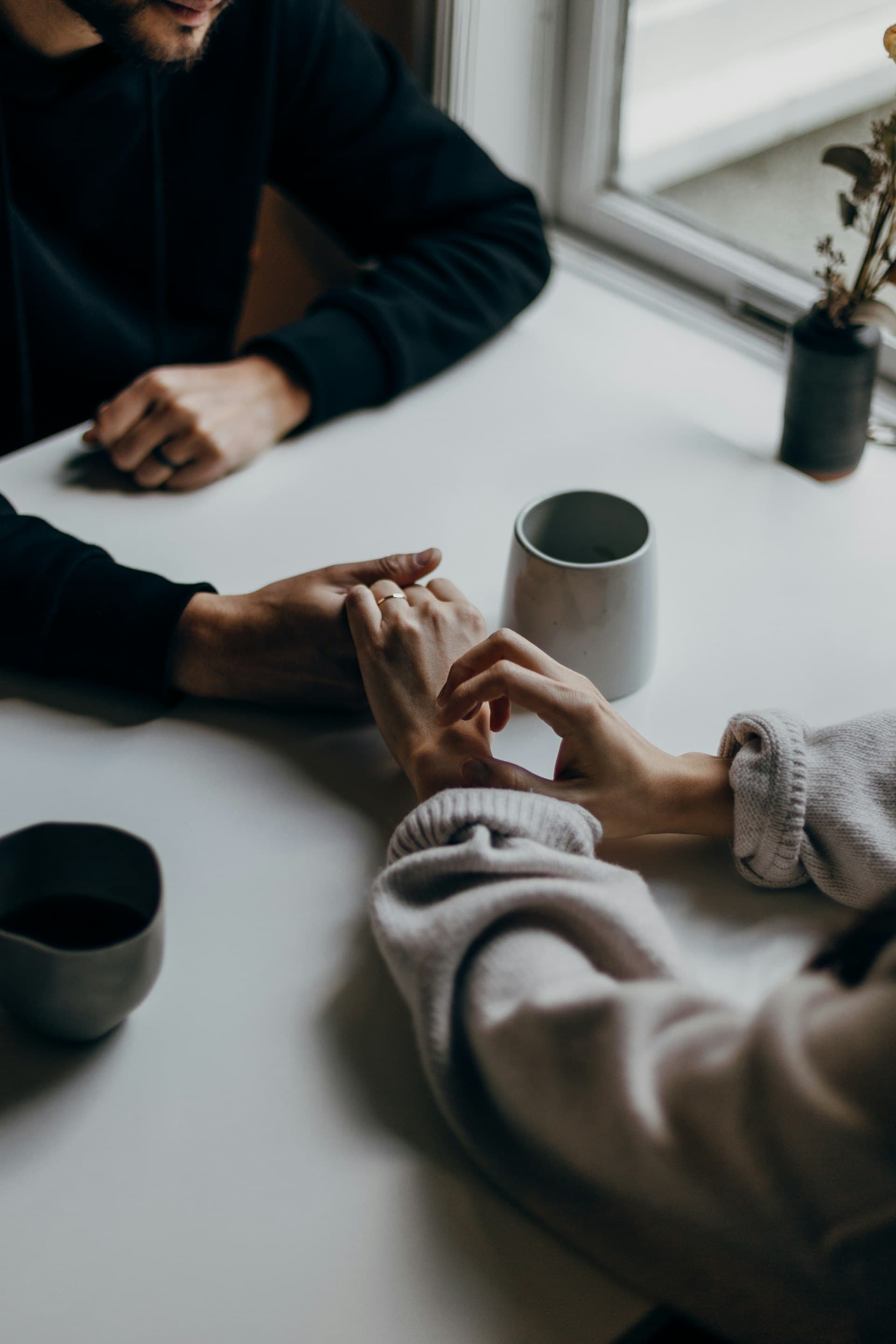 Two people's hands gently clasped across a table, a moment of reassurance